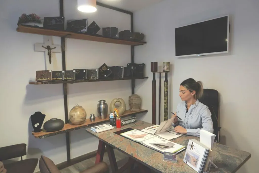 Conseillère funéraire travaillant à son bureau entourée d'urnes et plaques souvenirs.